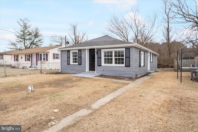 view of front of property featuring a shingled roof, fence, a front lawn, a trampoline, and a chimney