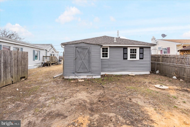 back of house with a storage shed, a fenced backyard, a shingled roof, and an outdoor structure