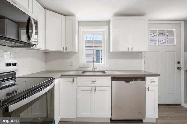 kitchen with appliances with stainless steel finishes, white cabinets, a sink, and decorative backsplash