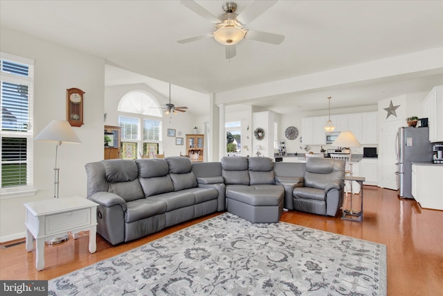 living area featuring vaulted ceiling, visible vents, a ceiling fan, and wood finished floors