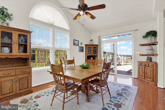 dining space with a ceiling fan, wood finished floors, baseboards, and high vaulted ceiling