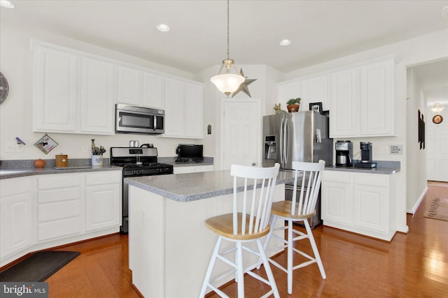 kitchen featuring white cabinetry, a kitchen bar, wood finished floors, and appliances with stainless steel finishes