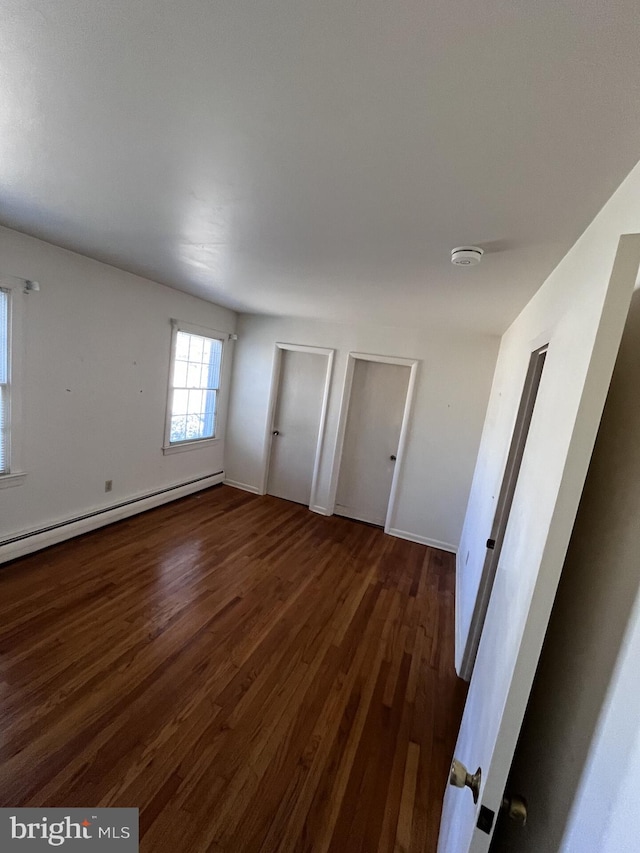 unfurnished bedroom with wood finished floors, baseboards, and baseboard heating