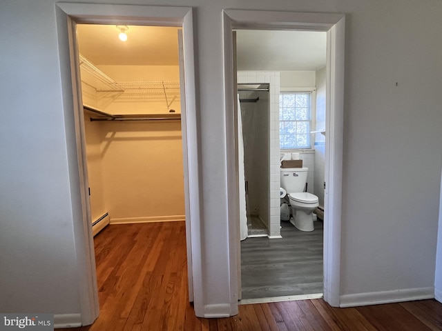 spacious closet featuring wood finished floors and a baseboard radiator