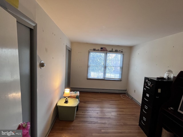 interior space featuring a baseboard heating unit, baseboards, and wood finished floors