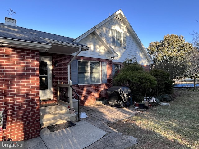 exterior space featuring brick siding and roof with shingles