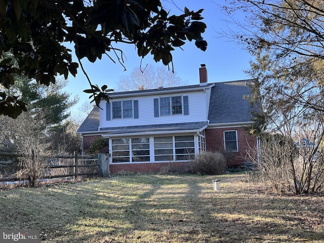 exterior space with a lawn, fence, a sunroom, brick siding, and a chimney