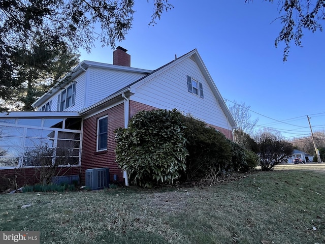 view of side of home with brick siding, central AC unit, a chimney, and a lawn