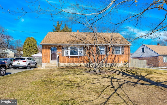 view of front of property with brick siding, a shingled roof, a front yard, and fence