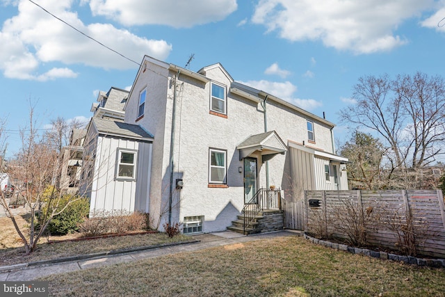 back of house featuring a yard, fence, board and batten siding, and stucco siding