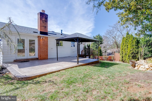 rear view of house with a lawn, a deck, fence, french doors, and a chimney