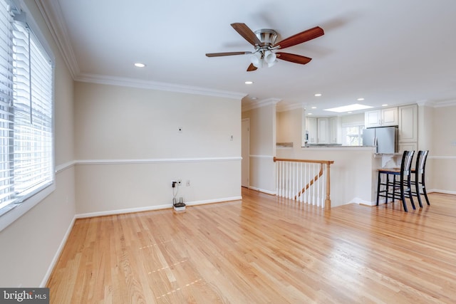 unfurnished living room with light wood-style flooring, crown molding, and baseboards