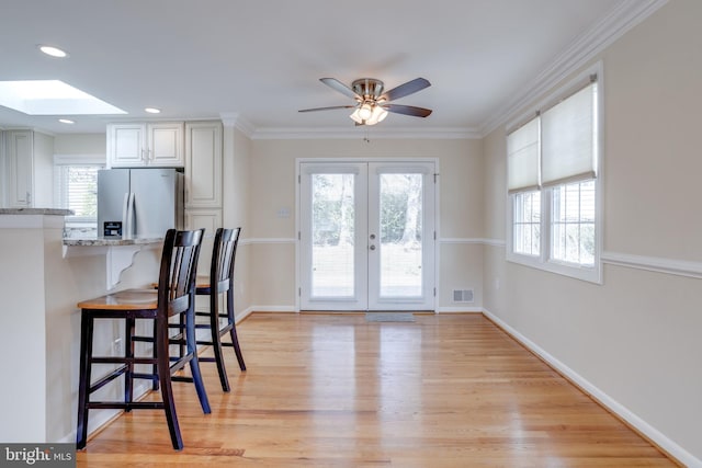 kitchen with baseboards, a breakfast bar area, light wood-type flooring, light stone counters, and stainless steel fridge