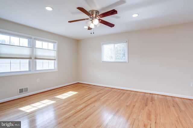 unfurnished room with wood finished floors, a healthy amount of sunlight, visible vents, and baseboards