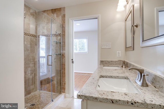 bathroom featuring a sink, baseboards, double vanity, and a shower stall