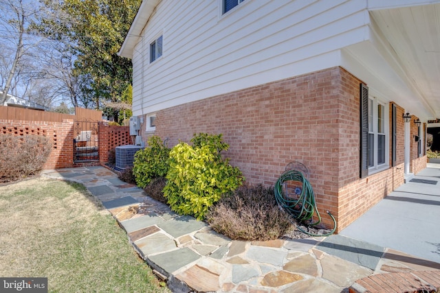 view of side of home featuring brick siding, central AC unit, and fence