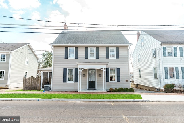 view of front of home with central air condition unit, roof with shingles, a chimney, and fence