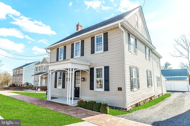 view of front of property with a porch, a front lawn, driveway, and a chimney