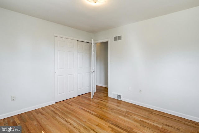 unfurnished bedroom featuring light wood-type flooring, visible vents, baseboards, and a closet