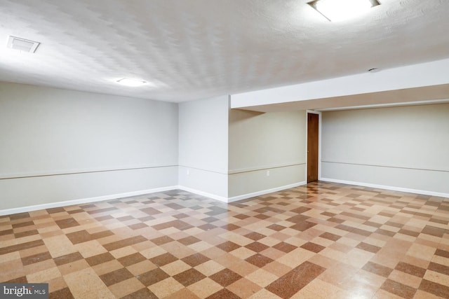 finished basement featuring visible vents, baseboards, and a textured ceiling