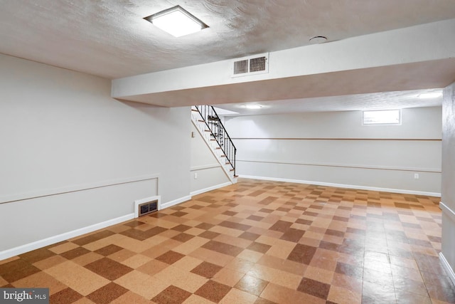 basement featuring stairs, baseboards, visible vents, and a textured ceiling