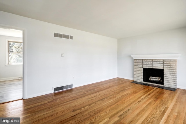 unfurnished living room with visible vents, a brick fireplace, and wood finished floors