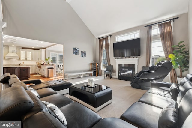 living area with a glass covered fireplace, light carpet, and high vaulted ceiling