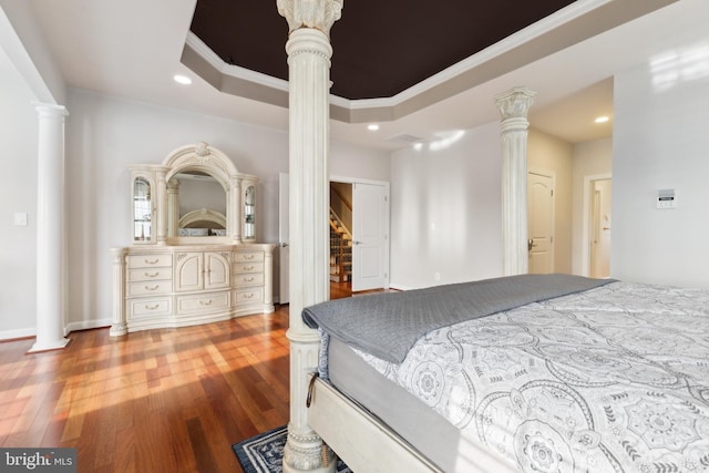 bedroom featuring a raised ceiling, decorative columns, wood finished floors, and recessed lighting
