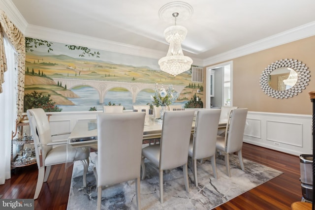 dining space featuring wood finished floors, ornamental molding, wainscoting, a decorative wall, and a notable chandelier