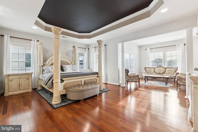 bedroom with visible vents, ornamental molding, wood-type flooring, decorative columns, and a raised ceiling