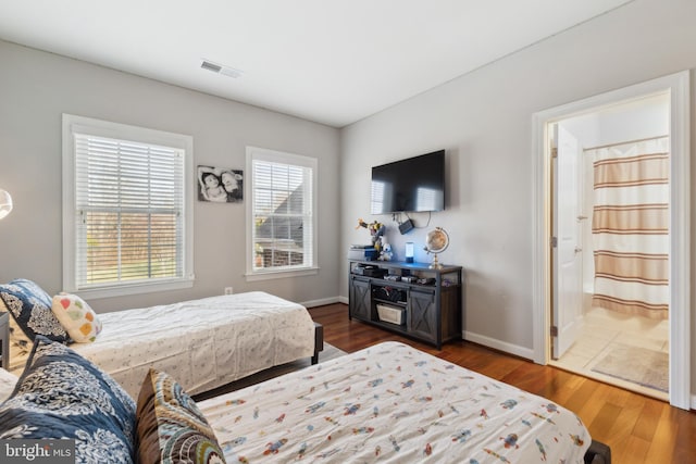 bedroom with connected bathroom, visible vents, baseboards, and dark wood-style floors