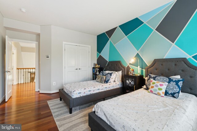 bedroom featuring a closet, baseboards, wood finished floors, and an accent wall