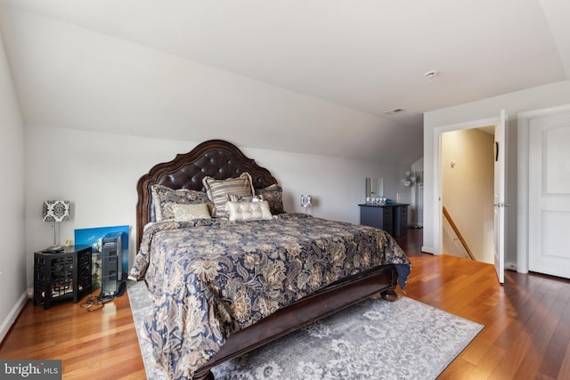 bedroom featuring vaulted ceiling, visible vents, baseboards, and hardwood / wood-style flooring
