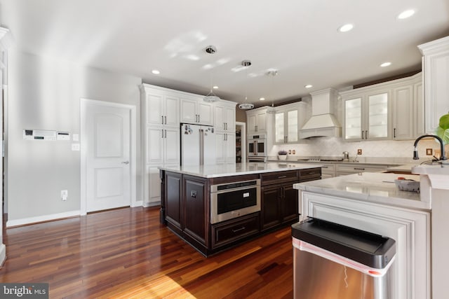 kitchen featuring high end fridge, dark wood-style flooring, a sink, custom range hood, and tasteful backsplash