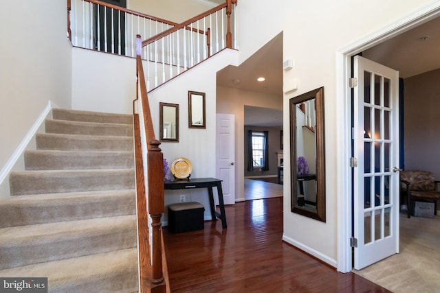 staircase with recessed lighting, a high ceiling, baseboards, and wood finished floors