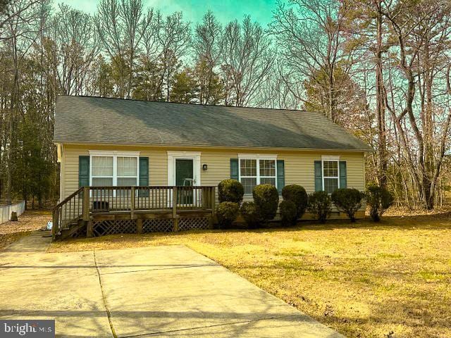 ranch-style house with a wooden deck, roof with shingles, and a front yard