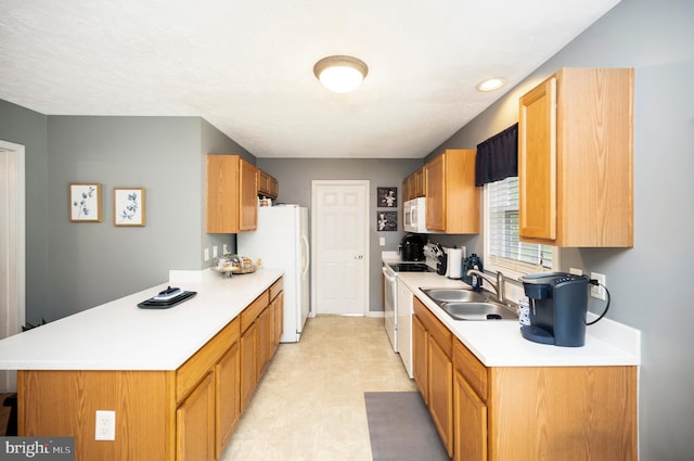 kitchen featuring a sink, white appliances, light floors, light countertops, and a peninsula