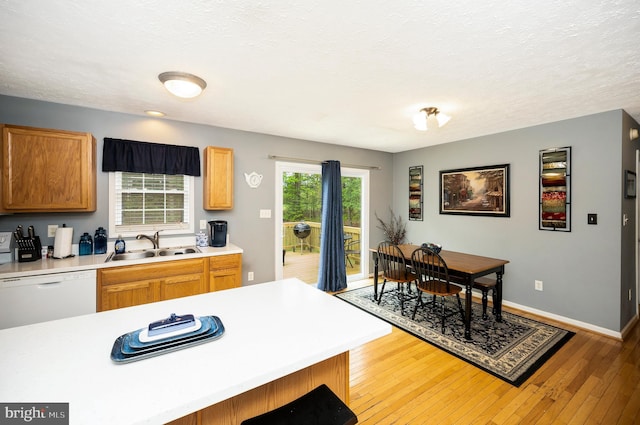 kitchen with a textured ceiling, a sink, dishwasher, light wood finished floors, and light countertops