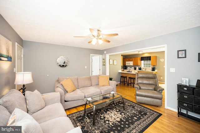 living area with a ceiling fan, baseboards, and light wood-style floors