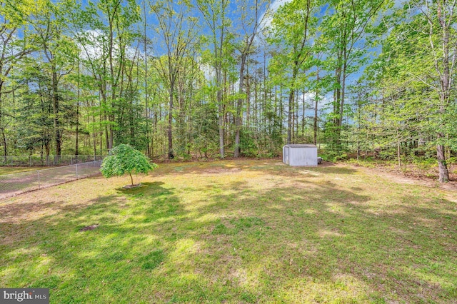 view of yard featuring fence, an outbuilding, a wooded view, and a storage unit