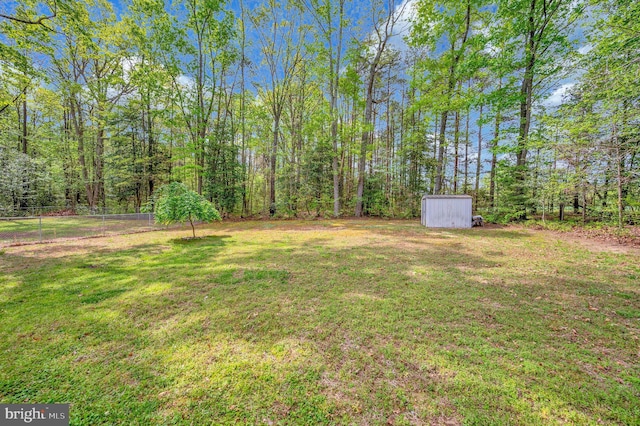 view of yard featuring an outdoor structure, a storage unit, a view of trees, and fence