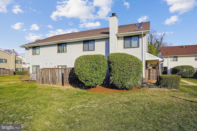 rear view of house featuring a lawn, a chimney, and fence