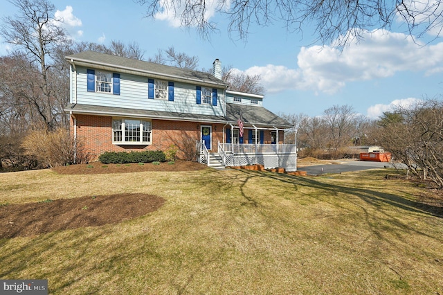 traditional home featuring a porch, brick siding, a front yard, and a chimney