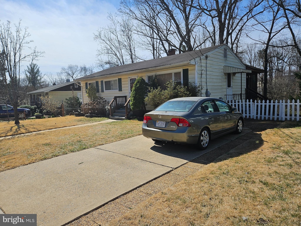 ranch-style house with concrete driveway, a chimney, a front yard, and fence