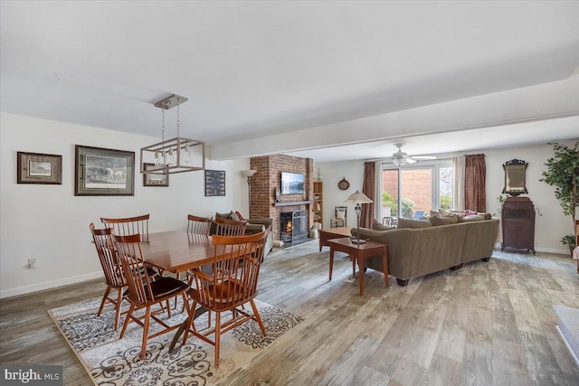 dining space featuring light wood-type flooring, baseboards, a brick fireplace, and ceiling fan with notable chandelier