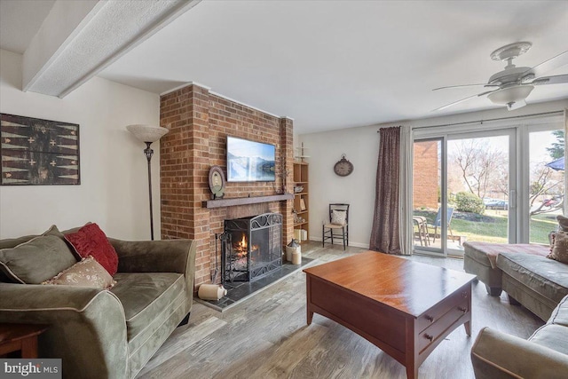 living area featuring a ceiling fan, wood finished floors, baseboards, beam ceiling, and a fireplace