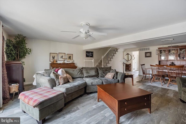 living room featuring stairway, visible vents, ceiling fan, and wood finished floors