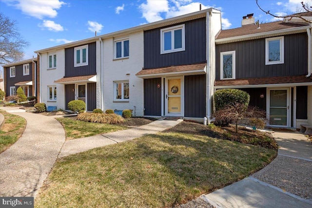 townhome / multi-family property with a front yard, brick siding, and a chimney