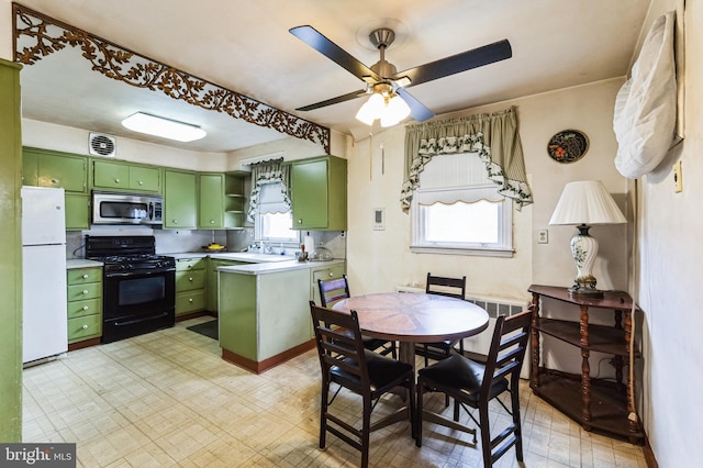 kitchen featuring black gas range oven, stainless steel microwave, light floors, freestanding refrigerator, and green cabinetry