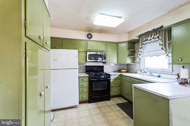 kitchen featuring a sink, stainless steel microwave, freestanding refrigerator, green cabinets, and black range with gas cooktop